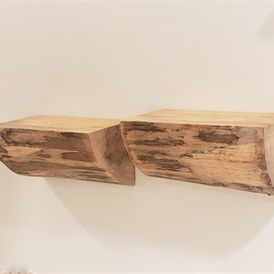 May include: Two wooden shelves made from tree trunks, with a natural wood finish and a curved edge. The shelves are mounted on a white wall.