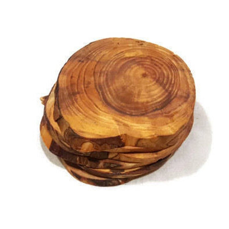 May include: A set of four round wooden coasters made from olive wood. The coasters are stacked on top of each other and have a natural wood grain pattern.