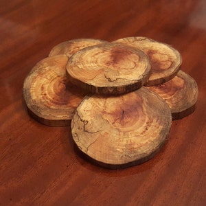 May include: A set of six natural wood coasters, each with a unique grain pattern. The coasters are stacked in a circular pattern, showcasing the natural beauty of the wood.
