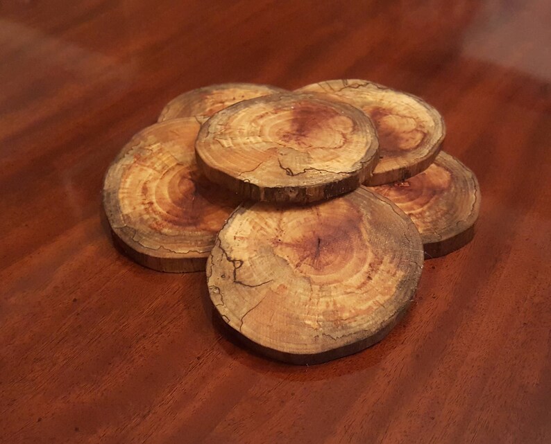 May include: A set of six natural wood coasters, each with a unique grain pattern. The coasters are stacked in a circular pattern, showcasing the natural beauty of the wood.