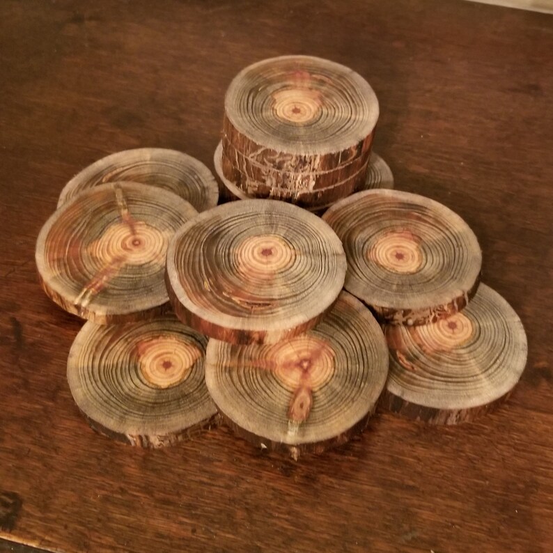 May include: A set of nine round wooden coasters with a natural wood finish. The coasters are made from tree slices and have a variety of grain patterns and colors, including brown, black, and orange.