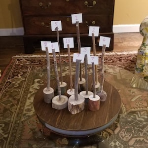 Puede incluir: Una mesa de madera con tapa de vidrio, que presenta un conjunto de 10 pequeños palos de madera con etiquetas de papel numeradas. Los palos están dispuestos en círculo sobre la mesa, con los números del 1 al 10 visibles.