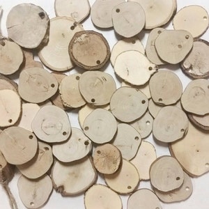 Może przedstawiać: Kolekcja małych, naturalnych plastr&oacute;w drewna w jasnobrązowym kolorze. Każdy plaster ma otw&oacute;r wywiercony w pobliżu g&oacute;rnej krawędzi, a usłojenie drewna jest widoczne. Te rustykalne drewniane krążki są idealne do rękodzieła i dekoracji.