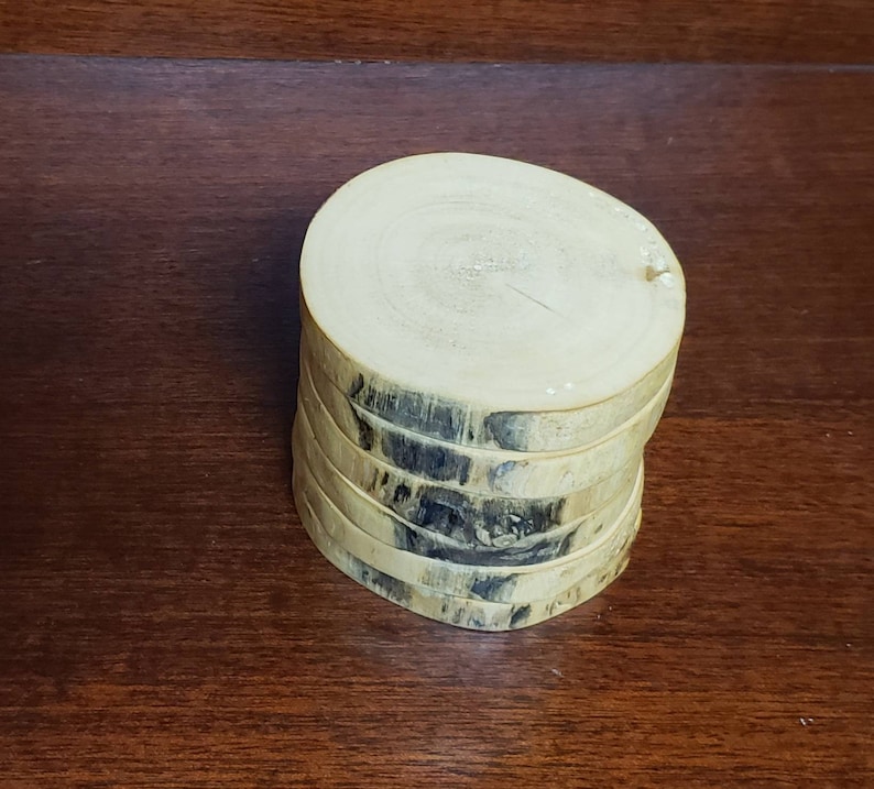 May include: A stack of six round wooden coasters with a natural wood finish. The coasters have a dark brown wood grain pattern.