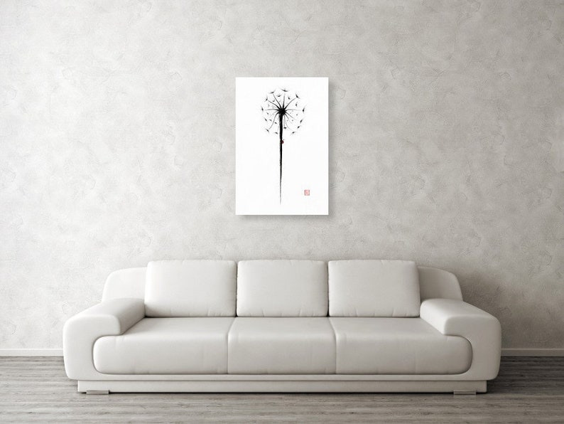 May include: A black and white dandelion art print on a white background. The dandelion is depicted in a minimalist style, with a long stem and a cluster of seeds. A small red square is in the lower right corner. The artwork is displayed on a white wall above a white sofa.