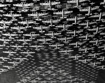 May include: A large collection of model airplanes suspended from a ceiling in a grid-like formation. The black and white image shows numerous small aircraft models, each featuring a star insignia on the wings, arranged in rows within a vast space.