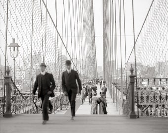 May include: A black and white photograph of people walking across the Brooklyn Bridge in New York City. The bridge is made of steel cables and towers. The people are dressed in clothing from the early 1900s.