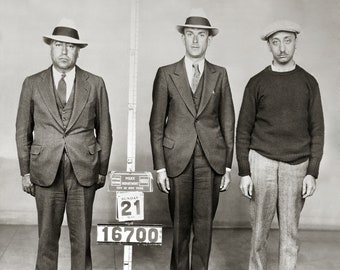 Peut inclure: Une photographie en noir et blanc de trois personnes dans une ligne de police. Deux portent des costumes et des fedoras, tandis que le troisième porte un pull et une casquette plate. Une toise affiche : POLICE DEPARTMENT CITY OF NEW YORK 1933 SUNDAY 21 MAY 16700.