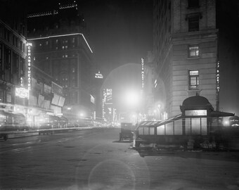 Peut inclure: Une vue nocturne en noir et blanc d'une rue urbaine avec une entrée de métro sur la droite. Des enseignes verticales lumineuses affichent du texte, notamment Cohan's Theatre, Hotel Albany, Black and White et Louis Martin, sous un lampadaire.