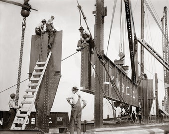 May include: A black and white photograph showing construction workers in hats and overalls assembling large riveted steel beams. One beam features the visible text "MLK IN BELL" and another shows "N ROS C". Cranes, cables, and a wooden ladder are present.
