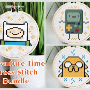 Op de afbeelding: Een kruissteekbundel met drie Adventure Time-personages: Finn, BMO en Jake. Elk personage is geborduurd op witte stof in een houten borduurring. De tekst "Adventure Time Cross Stitch Bundle" wordt hieronder weergegeven.