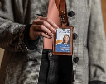 May include: A brown leather ID badge holder with a matching leather lanyard. The holder features a clear plastic window displaying an identification card for Cedar Elementary School with the name Lisa Anderson and the title 3rd Grade Teacher.
