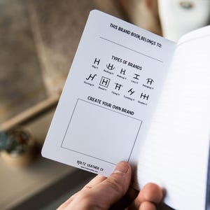 May include: A white page from a notebook with black text that reads THIS BRAND BOOK BELONGS TO, followed by a list of brand types like Reg H, Rocking H, and Walking H. Below is a box labeled CREATE YOUR OWN BRAND and the Holtz Leather Co logo.