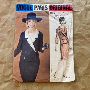 May include: Vintage Vogue Paris Original sewing pattern number 1376 by Jacques Heim. The pattern features two designs for a double-breasted suit with a skirt. One design is black with a white collar and the other is a pink and white patterned fabric.
