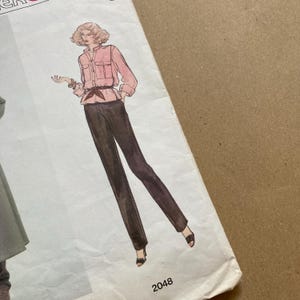 May include: A vintage sewing pattern featuring a woman wearing a pink blouse with a belt and brown trousers. The pattern number is 2048.