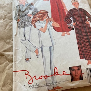 Op de afbeelding: Vintage naaipatroon met illustraties van nachtkledingontwerpen. Het patroon bevat tekeningen van een gestreepte pyjamaset, een rode nachtjapon en een geruite badjas. De merknaam "Brooke" is zichtbaar, samen met een foto van Brooke Shields.