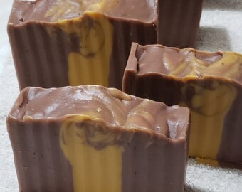May include: Four bars of handmade soap with a brown and yellow swirl pattern. The soap is arranged in a stack on a white towel.