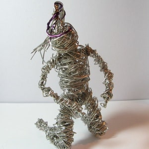 Puede incluir: Una escultura de alambre plateado de una persona arrodillada con un detalle de alambre morado en la cabeza.