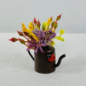 May include: A small brown metal teapot with a ladybug design, filled with a bouquet of yellow, purple, and green flowers.