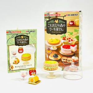 Könnte beinhalten: Miniatur-Kuchenladen-Set mit Schachteln und einzelnen Kuchen. Die Schachteln zeigen japanischen Text und Illustrationen von Kuchen. Einzelne Kuchen sind ein grüner Kuchen auf einem Sockel und eine gelbe Kuchenrolle.