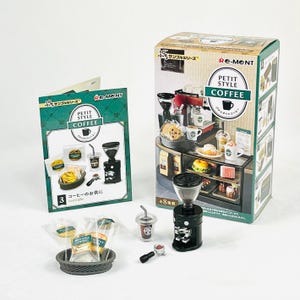 May include: A miniature coffee shop set with a black coffee grinder, a clear plastic cup with a straw, and a small espresso machine. The set includes a box with the words "PETIT STYLE COFFEE" and a green and white card with the same text.