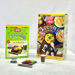 Könnte beinhalten: Ein Set mit Miniatur-Lebensmitteln aus der japanischen Spielzeuglinie Re-Ment. Das Set enthält eine Miniaturdose Corned Beef, einen Teller mit einem Miniatur-Hamburger, Essstäbchen und ein Miniatur-Glas Eiskaffee. Die Schachtel zeigt eine farbenfrohe Illustration verschiedener japanischer Lebensmittel.