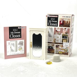 Puede incluir: Un armario blanco en miniatura con puerta de espejo, una caja y un folleto. La caja y el folleto presentan el texto "My Sweet Closet" en inglés y japonés. La caja muestra imágenes de accesorios en miniatura.
