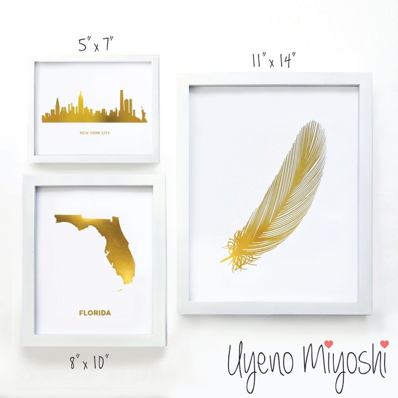 Pu&ograve; includere: Tre stampe incorniciate con disegni in foglia d'oro. La stampa superiore misura 5 pollici per 7 pollici e presenta uno skyline della citt&agrave; di New York in foglia d'oro. La stampa centrale misura 8 pollici per 10 pollici e presenta un contorno dello stato della Florida in foglia d'oro. La stampa inferiore misura 11 pollici per 14 pollici e presenta una piuma in foglia d'oro. Le stampe sono tutte incorniciate in bianco.