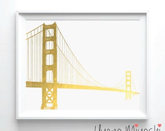 May include: A gold foil print of the Golden Gate Bridge on a white background. The print is framed in a white frame. The artist's signature, "Uyeno Miyoshi", is printed in black at the bottom of the print.