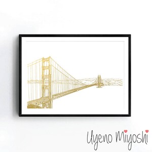 May include: A gold foil print of the Golden Gate Bridge in San Francisco, California. The bridge is depicted in a minimalist line drawing style against a white background.