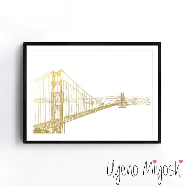 May include: A gold foil print of the Golden Gate Bridge in San Francisco, California. The bridge is depicted in a minimalist line drawing style against a white background.