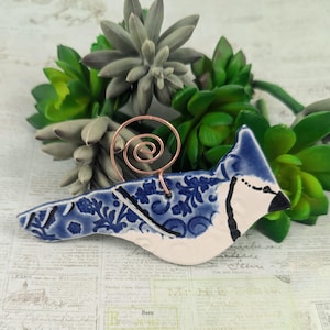 May include: Blue and white ceramic bird ornament with a floral pattern. The bird has a copper wire hanger.