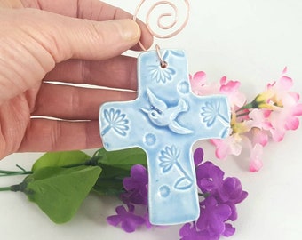 May include: A light blue ceramic cross with a hummingbird design and floral accents. The cross has a copper wire hanger.