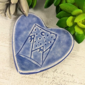 May include: A blue heart-shaped ceramic dish with a white design of mountains, a crescent moon, and stars.