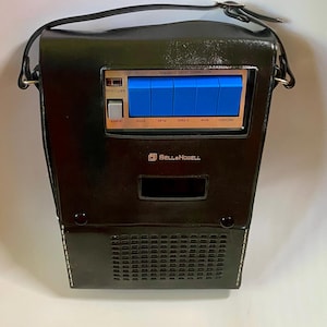 May include: Black vintage Bell & Howell portable tape recorder with a carrying handle. The recorder has blue buttons and the words "STOP", "PLAY", "FFWD", "REW", and "RECORD". The front has a speaker grill and the Bell & Howell logo.