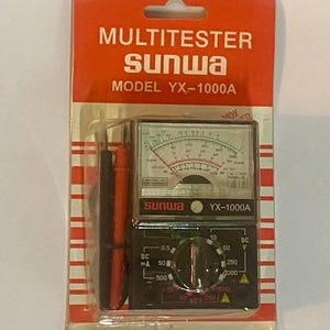 May include: A red and white package containing a black and silver Sunwa YX-1000A multimeter. The multimeter has two dials and a needle gauge. The package says "MULTITESTER sunwa MODEL YX-1000A NEW ED".