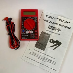 May include: A red Cen-Tech digital multimeter with black and red test leads and an instruction manual. The multimeter has a rotary dial and a digital display. The instruction manual is white with black text and a diagram of the multimeter.