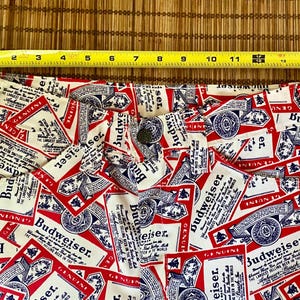 May include: Close-up of white fabric with a repeating pattern of red and blue Budweiser beer labels. The labels feature the Budweiser logo and text. The fabric is likely part of a pair of shorts or pants.