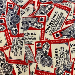 May include: Close-up of a fabric with a repeating pattern of Budweiser beer labels. The labels are red, white, and blue, featuring the Budweiser logo and text. The design is a collage of overlapping labels.