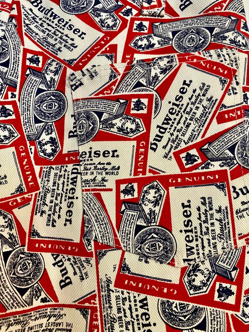 May include: Close-up of a fabric with a repeating pattern of Budweiser beer labels. The labels are red, white, and blue, featuring the Budweiser logo and text. The design is a collage of overlapping labels.
