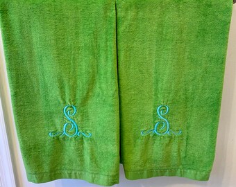 May include: Two green towels with blue embroidered letter S's on them. The towels are hanging on a towel rack.