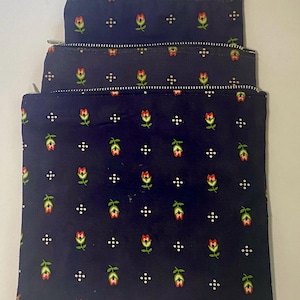 May include: Three zippered pouches with a navy blue background and a white and red floral pattern. The pouches are stacked on top of each other.