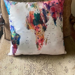 May include: A white throw pillow with a colorful watercolor world map design. The map is painted in shades of pink, purple, blue, green, and orange.