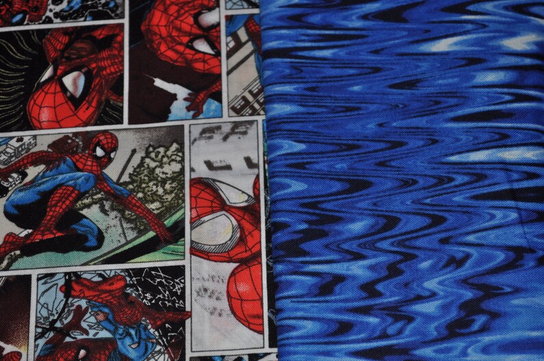 Puede incluir: Una tela azul y negra con un patr&oacute;n ondulado. La tela est&aacute; impresa con una imagen de estilo c&oacute;mic de Spiderman en rojo y azul.