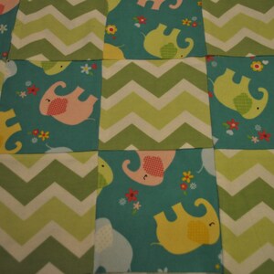 May include: A teal blue fabric with a patchwork design featuring green and white chevron patterns and pink, yellow, and green elephants with floral accents.