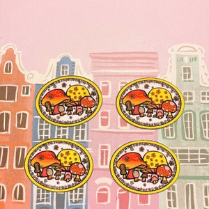 May include: Four yellow and orange mushroom-shaped coasters with a floral design. Each coaster features a group of three mushrooms with red and white polka dots.