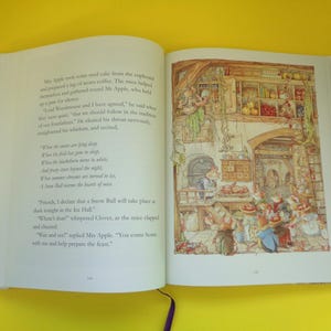 May include: An open book with colorful illustrations. The right page shows a detailed drawing of a kitchen scene with mice preparing food. The left page has printed text. The book is on a yellow surface.
