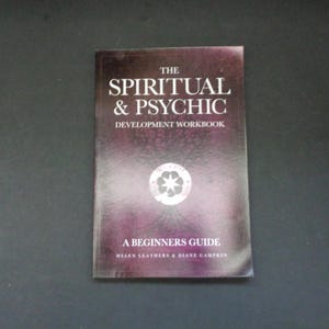 May include: A book titled "The Spiritual & Psychic Development Workbook" with a purple and white cover. The cover features the title in large white letters, a circular emblem, and the subtitle "A Beginners Guide".