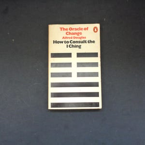 May include: A vintage paperback book titled "The Oracle of Change: How to Consult the I Ching" by Alfred Douglas. The cover features a cream-colored background with black and white horizontal lines and red text.