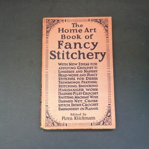 Può includere: Un libro vintage intitolato "The Home Art Book of Fancy Stitchery" con una copertina color pesca e un bordo floreale. Il libro elenca varie tecniche di cucito, tra cui uncinetto, maglia e ricamo. A cura di Flora Klickmann.